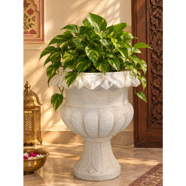 18-inch handcrafted white marble urn planter with fluted detailing resting on an ornate pedestal stand supported by carved crane sculptures, placed near a wooden door on a tiled patio.